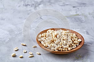 Peanuts in wooden plate over white textured background, top view, close-up.