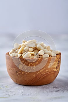 Peanuts in wooden plate over white textured background, top view, close-up.