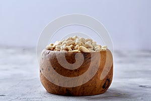 Peanuts in wooden plate over white textured background, top view, close-up.