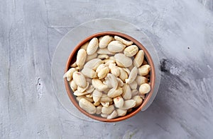 Peanuts in wooden plate over white textured background, top view, close-up.