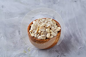 Peanuts in wooden plate over white textured background, top view, close-up.