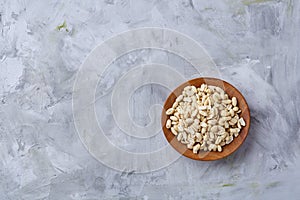 Peanuts in wooden plate over white textured background, top view, close-up.