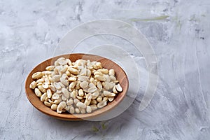 Peanuts in wooden plate over white textured background, top view, close-up.