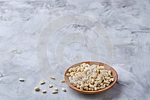 Peanuts in wooden plate over white textured background, top view, close-up.