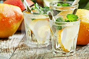 Pear cocktail with soda, fruit slices and mint on an old wooden