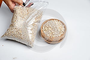 Pearl barley grains in a wooden bowl and a transparent bag on a white background