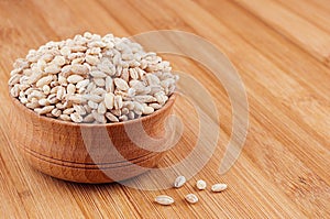 Pearl barley in wooden bowl on brown bamboo board, closeup. Healthy dietary cereals background.