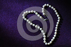 Pearl beads in heart shape on purple velvet background