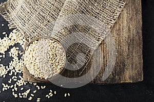 Pearl dry cereal in a vintage wooden bowl on a plain dark background for text placement and advertising. Selective focus