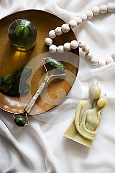 Pearl necklace, a green gua sha laying on top of white clean sheets, cozy atmoshpere