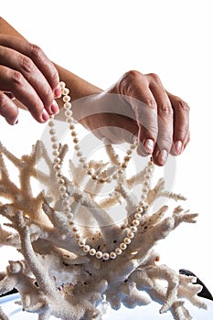 A pearl necklace in her hands against the backdrop of coral