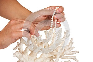 A pearl necklace in her hands against the backdrop of coral