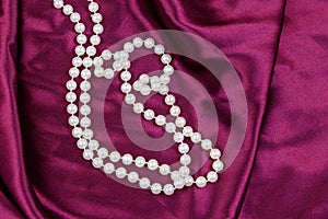 Pearl necklace on purple satin fabric background