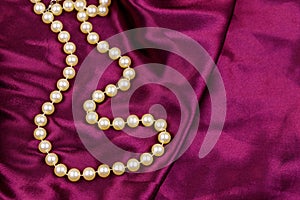 Pearl necklace on purple satin fabric background