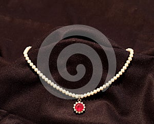 Pearl necklace with red ruby stone in black background