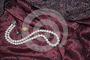 Pearl necklace, rose brooch on dark cherry silk