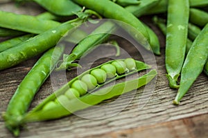 Peas in a pod shot on wood one open with visible peas.