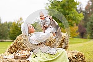 Peasant mother with little baby in summer playing on haystack in the field