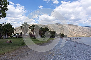 pebble beach on the Gulf of Corinth, palm trees, sea, mountains, sky with clouds, Greece