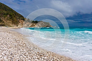 Pebble beach, stormy blue sea, green hill and gray sky in Dominican Republic