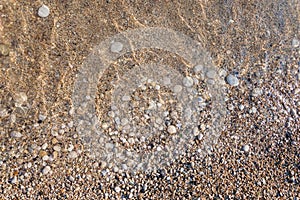 Pebble beach textured background. Close-up of crystal clear water with round stones and sand on Mediterranean sea