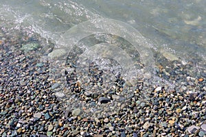 Pebble coastline. Seashore with transparent water and small stones