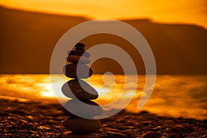 Pebble pyramid silhouette on the beach. Sunset with sea in the background. Zen stones on the sea beach concept