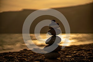 Pebble pyramid silhouette on the beach. Sunset with sea in the background. Zen stones on the sea beach concept