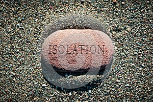 Pebble stone alone on sand with word Isolation carved on it in a conceptual image