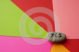 Pebble stone with text yes on them. Colorful background from sheets of paper