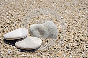 Pebble stones in the sand, one stone has heart shape