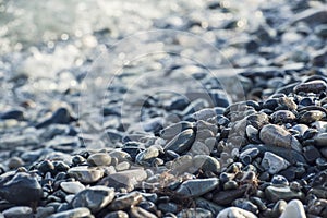 Pebble stones on the shore close up in the blurry sunset light in the distance background