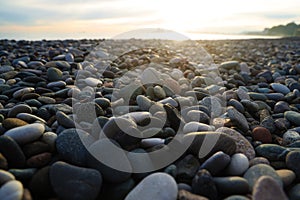 Pebble stones on the shore close up in the blurry sunset light in the distance background. sunrays. Pebble stones on sea shore.