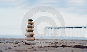 Pebble tower by the seaside with blurry pier down to the sea Stack of zen rock stones on the sand Stones pyramid on the beach