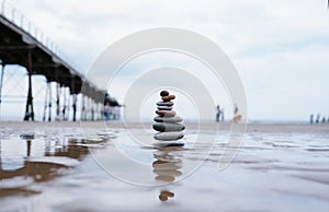 Pebble tower by seaside with blurry pier down to the sea, Stack of Zen rock stones on the sand, Stones pyramid on the beach