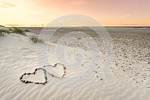 Pebbles arranged in shape of two hearts on sand beach ripples with beautiful sunset.