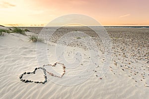 Pebbles arranged in shape of two hearts on sand beach ripples with beautiful sunset. photo