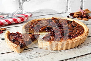 Pecan cranberry pie with slice removed on white wood