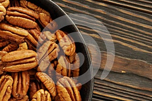 Pecan nuts in a bowl close up on brown wooden table background.