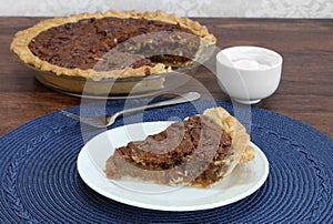 Pecan pie slice with whole pie in background.