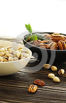 Pecan and pistachios nuts in a bowls  close up on brown wooden table background