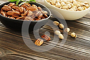 Pecan and pistachios nuts in a bowls  close up on brown wooden table background