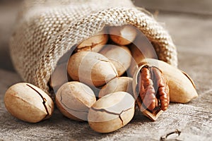 Pecans spill out of a bag on a wooden table, close-up. Peeled, in a shell