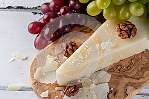 Pecorino romano, hard italian sheep milk cheese on wooden cutting board with grape, selective focus