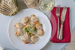 Pecten maximus cooked in the white wine on the white plate, vintage cutlery on the red napkin, glass of white wine