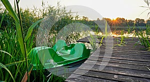 Pedal bike tied down to wooden pier. Sunrise over the lake. Landscape at the lake with reeds. Orange sky.