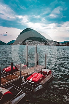 Pedal boats near a wooden dock on the sea surrounded by beautiful green mountains under cloudy sky