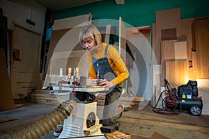 Pedant woman joiner works in joinery workshop, sanding, turning wooden knife blanks on lathe