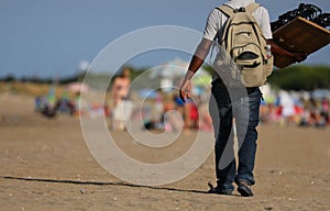 peddler with long pants walking on the sunny beach looking to se