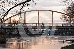 Pedestrian bridge with arches over frozen river against evening